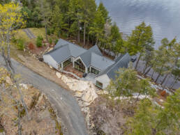 Aerial view of a lakeside house, nestled along the water's edge amidst natural surroundings.