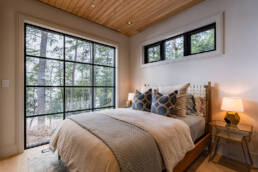 A serene bedroom featuring a bed and large windows that offer a view of the tranquil woods outside.