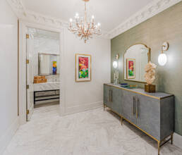 A luxurious hallway featuring a textured gray console with gold accents, framed modern art, a sculptural bust, and a sparkling chandelier, exemplifying interior design photography for the Hazelton Residence.