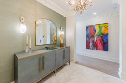 A sophisticated hallway with a textured gray console, gold hardware, a sculptural bust, wall sconces, and a vibrant abstract painting, captured to showcase interior design photography for the Hazelton Residence.