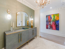 A sophisticated hallway with a textured gray console, gold hardware, a sculptural bust, wall sconces, and a vibrant abstract painting, captured to showcase interior design photography for the Hazelton Residence.