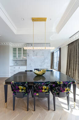 Contemporary dining area with a dark wood table, floral-upholstered chairs, marble backsplash, and sleek lighting, showcased with interior design photography.