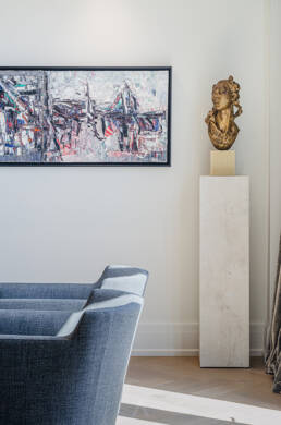 Modern living space featuring abstract wall art, a classical bust on a pedestal, and a sleek blue chair, captured through interior design photography.