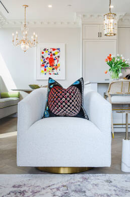 White swivel chair with a colorful patterned pillow, abstract wall art, and floral decor, captured with interior design photography.