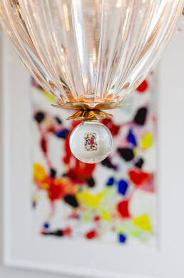 Crystal chandelier detail with gold accents and colorful abstract art in the background, highlighted by through interior design photography.