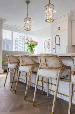 Bright kitchen island with cane-back barstools, gold accents, floral centerpiece, and pendant lighting, captured through interior design photography.