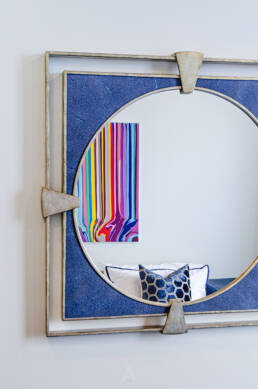 A modern circular mirror reflecting a vibrant striped painting and geometric pillow, highlighted by interior design photography.